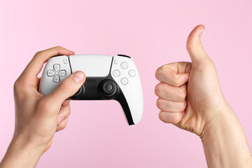 Man using wireless game controller and showing thumbs up on pink background, closeup