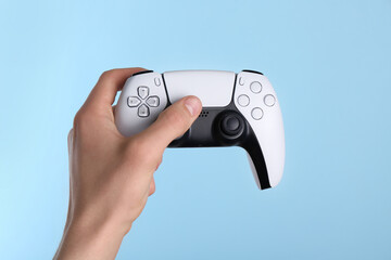 Man using wireless game controller on light blue background, closeup