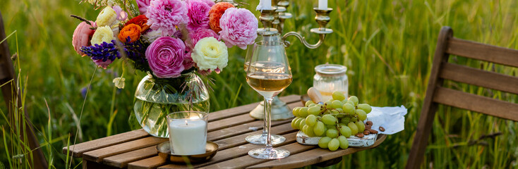 Elegant wedding or private party for a loving couple table setting outdoors in the garden. Beautiful decor with fresh ranunculi flowers, candles. Gourmet cheese board, fruits, white wine. Banner