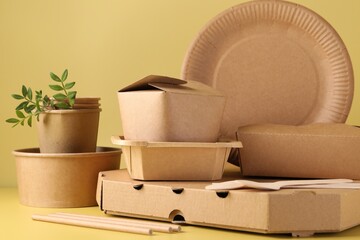 Eco friendly food packaging. Paper containers, tableware and green twigs on pale yellow background
