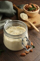 Fresh almond flour in jar and nuts on wooden table, closeup