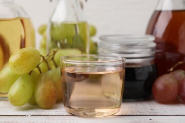 Different types of vinegar and grapes on wooden table, closeup
