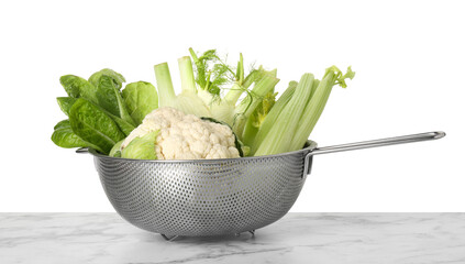Metal colander with different vegetables on marble table against white background