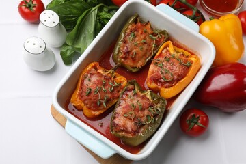 Tasty stuffed peppers in dish and ingredients on white tiled table, above view