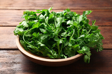 Fresh coriander in bowl on wooden table, closeup