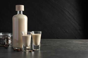 Coffee cream liqueur in glasses, bottle and beans on grey table, space for text