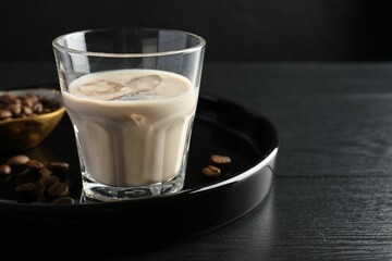Coffee cream liqueur in glass and beans on black wooden table, space for text