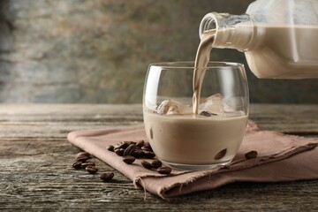 Pouring coffee cream liqueur into glass at wooden table, closeup