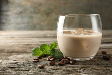 Coffee cream liqueur in glass, mint and beans on wooden table, closeup. Space for text