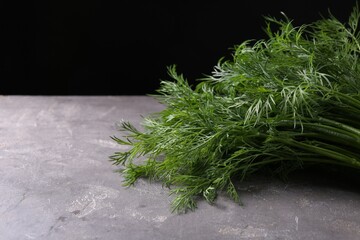 Sprigs of fresh dill on grey textured table against black background, closeup. Space for text