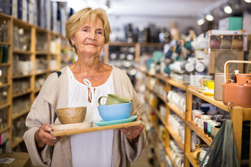 Portrait of focused mature woman buyer choosing dishes at decor store