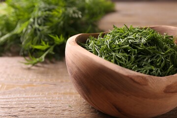 Fresh cut dill in bowl on wooden table, closeup. Space for text