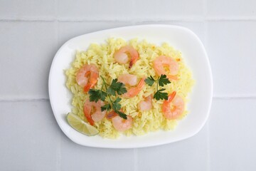 Delicious risotto with shrimps, lime and parsley on white tiled table, top view