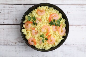 Delicious risotto with shrimps and parsley in bowl on white wooden table, top view