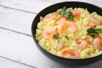 Delicious risotto with shrimps and parsley in bowl on white wooden table, closeup. Space for text