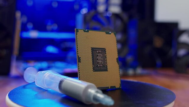 Computer processor with thermal paste rotates close up. Modern computer part with PC case on background. Building personal gaming and workstation pc concept