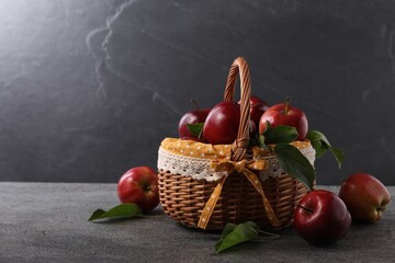 Ripe red apples and leaves in wicker basket on dark grey table. Space for text