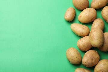 Fresh raw potatoes on green background, flat lay. Space for text