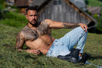 Portrait of sexy farmer or cowboy with muscular torso on hay field in countryside. Rural USA, rural America. Male model in american countryside landscape nature on ranch or farm, USA.