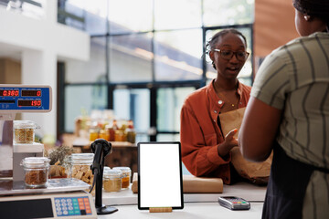A lady wearing glasses converses with a vendor at the payment counter, while a digital device...