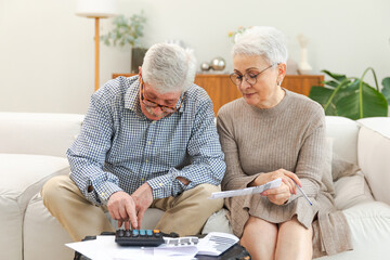 Middle aged senior couple sit with laptop and paper document. Older mature man woman reading paper...