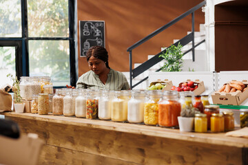 African american customer looking around grocery store, browsing fresh, locally grown produce and sustainable packaging. Female client checking variety of organic bio products in glass jars.