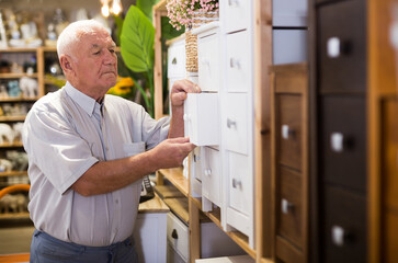 Portrait of elderly man choosing wooden chest of drawers in a furniture store
