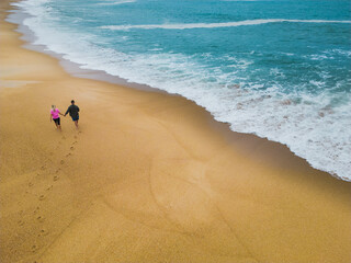 A young couple walks on the beach of Nazaré during the waves on a spring day, drone point of view