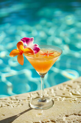 A bright orange cocktail decorated with tropical flowers by the blue pool