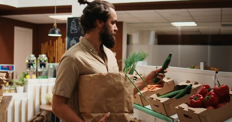Man in zero waste shop buying vegetables, checking products before making purchase decision to...