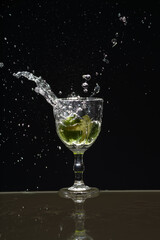 Lemon falling into a glass of transparent water causing splashes upwards. Isolated on gray background.