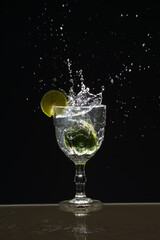 Splashes coming out of a glass cup with clear water caused by a slice of lemon. Isolated on dark background.