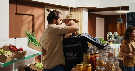 Deliveryman arriving in sustainable supermarket to pick up organic food order for client. Man...