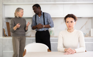 Adult upset woman sitting in kitchen during family quarrel between elderly woman and adult man