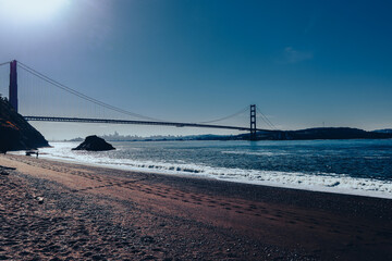 Panoramic view of the San Francisco Bay and Golden Gate Bridge from a sandy beach. Downtown San Francisco silhouette emerging in the distance and the sky is a deep blue, bathed in sunshine.