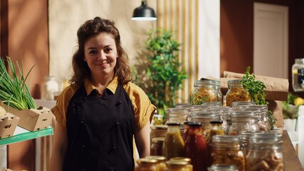 Portrait of smiling zero waste supermarket owner using nonpolluting glass containers for its bulk items to lower climate impact. Joyful trader in local grocery shop arranging merchandise