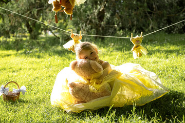 Girl cuddling teddy bear on grass under clothesline.