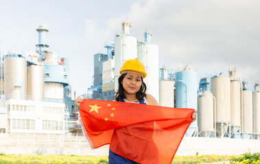 Teenage girl in blue overalls waving the flag of China against backdrop of a modern metallurgical...