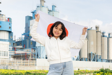 Happy young woman holding big flag of Japan against background of factory