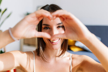 Portrait of smiling attractive young woman making heart shape with hands. Love sign