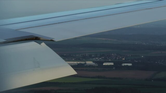 Flying airplane wing with flap in sky over countryside lands closeup. Aircraft vehicle part view out of window. Travelling abroad by plane