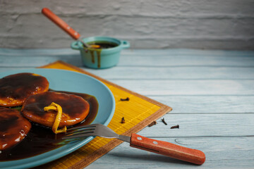Sopaipillas in a blue plate with an orange peel on top. Utensils, cinnamon stick, cloves and a...