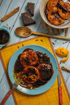 Sopaipillas pasadas on a blue plate with orange peel on a yellow placemat with utensils. Aerial view with more sopaipillas, chancaca, cinnamon, cloves, and wooden ladle. Comida t&iacute;pica chilena.
