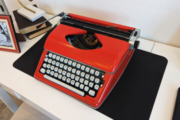 Angled overhead view of white desk workplace with bright red vintage typewriter