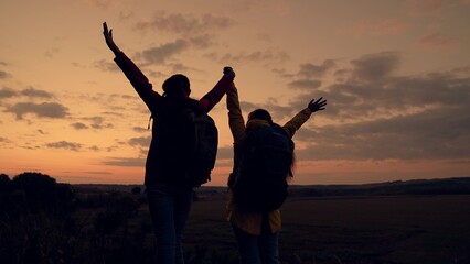 Two travel woman backpacker winner friends raising hands on mountain peak, sunset. Active extreme...