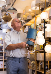 Portrait of mature man customer choosing table lamp at store of household goods