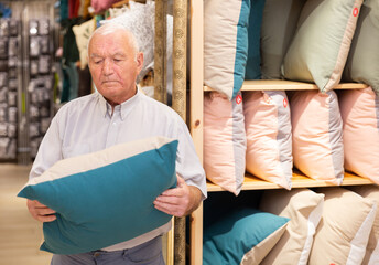 Focused elderly man choosing decorative pillow at household store