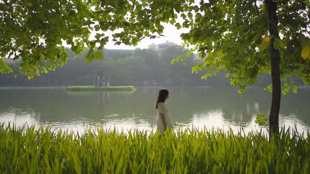 Portrait of happy Asian Vietnamese woman travel at Turtle tower in river of Hoan Kiem Lake in public park garden in Downtown Hanoi. Urban city, Vietnam. People lifestyle.