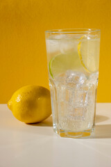 Glass ice lemonade on yellow background. Minimal style composition summer drink.