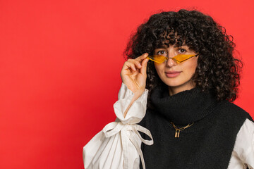 Stylish smiling Caucasian young woman with curly hair wearing orange sunglasses glad expression...